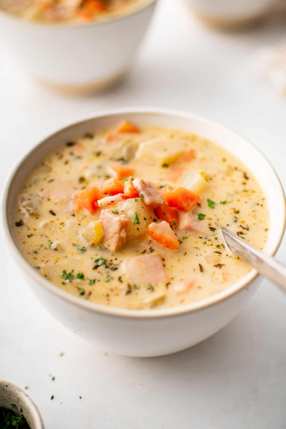 zuppa di patate e prosciutto in una ciotola bianca con un cucchiaio