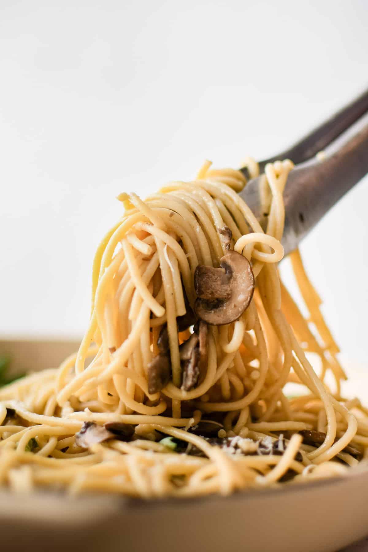 Pasta ai funghi con aglio e burro sollevata dalla padella con delle pinze