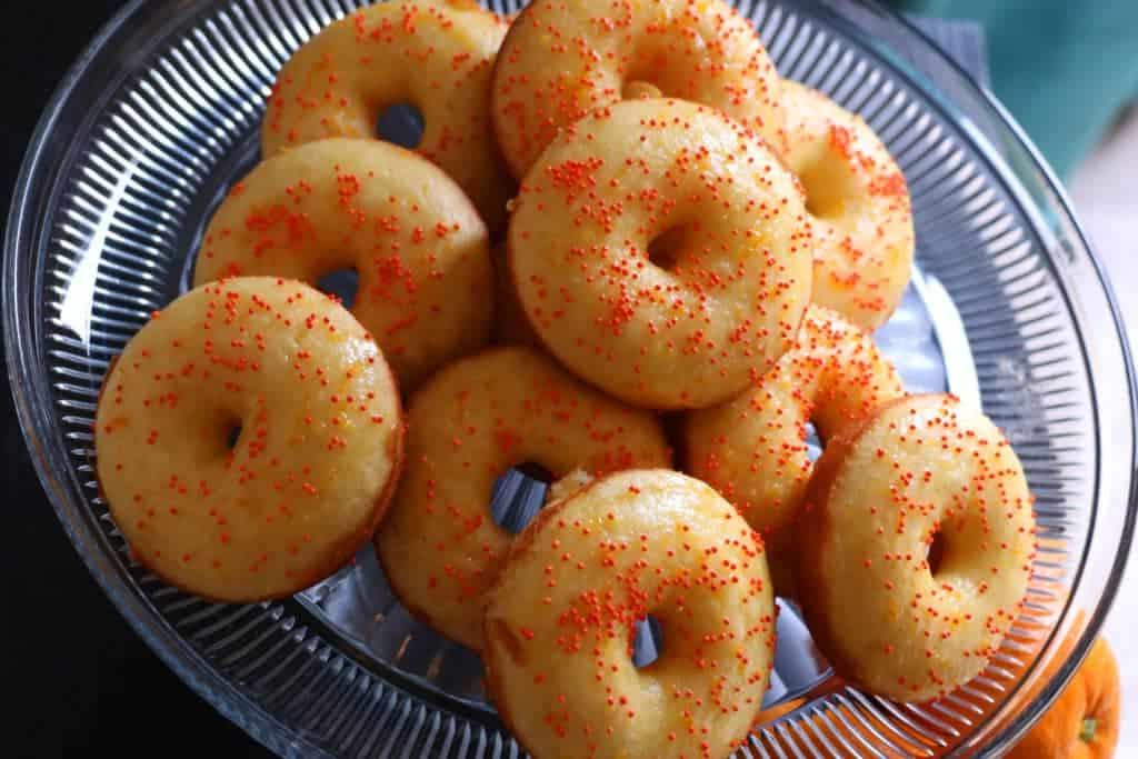 Primo piano di una ciambella all'arancia glassata con spruzzini, su un piatto.