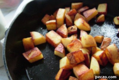 Diced Yukon Gold potatoes sizzling in a skillet with olive oil, browning beautifully, indicating they are almost ready.