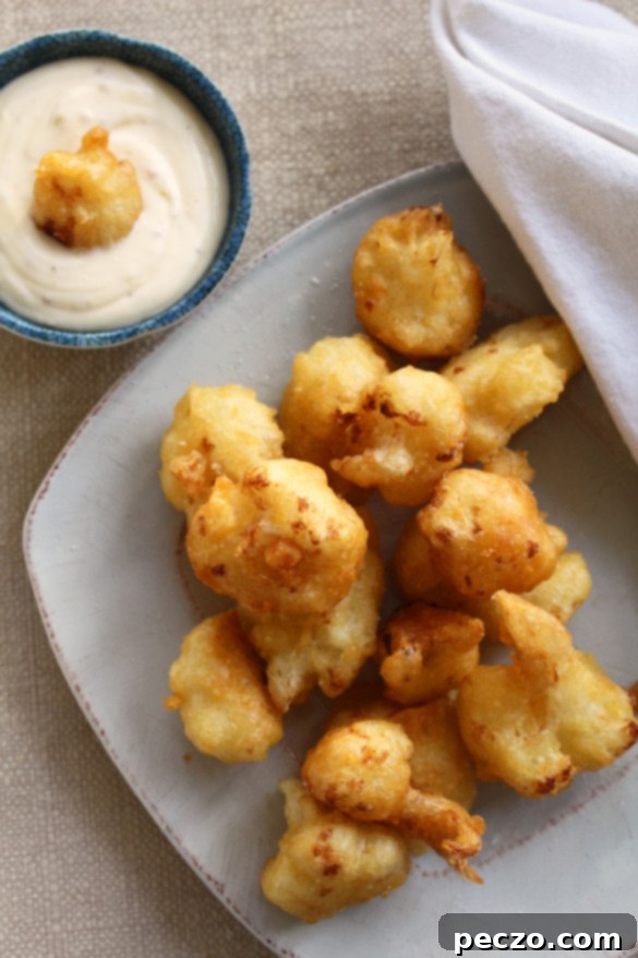 Golden-brown, crispy cauliflower fritters served on a platter with a side of lemony mayonnaise for dipping.