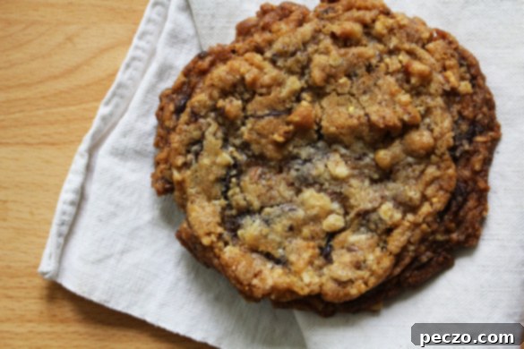 A stack of perfectly baked Mona's Mother's Best Friend's Favourite Cookies on a rustic wooden board, with a few extra cookies scattered around, showcasing their golden-brown edges and soft centers.