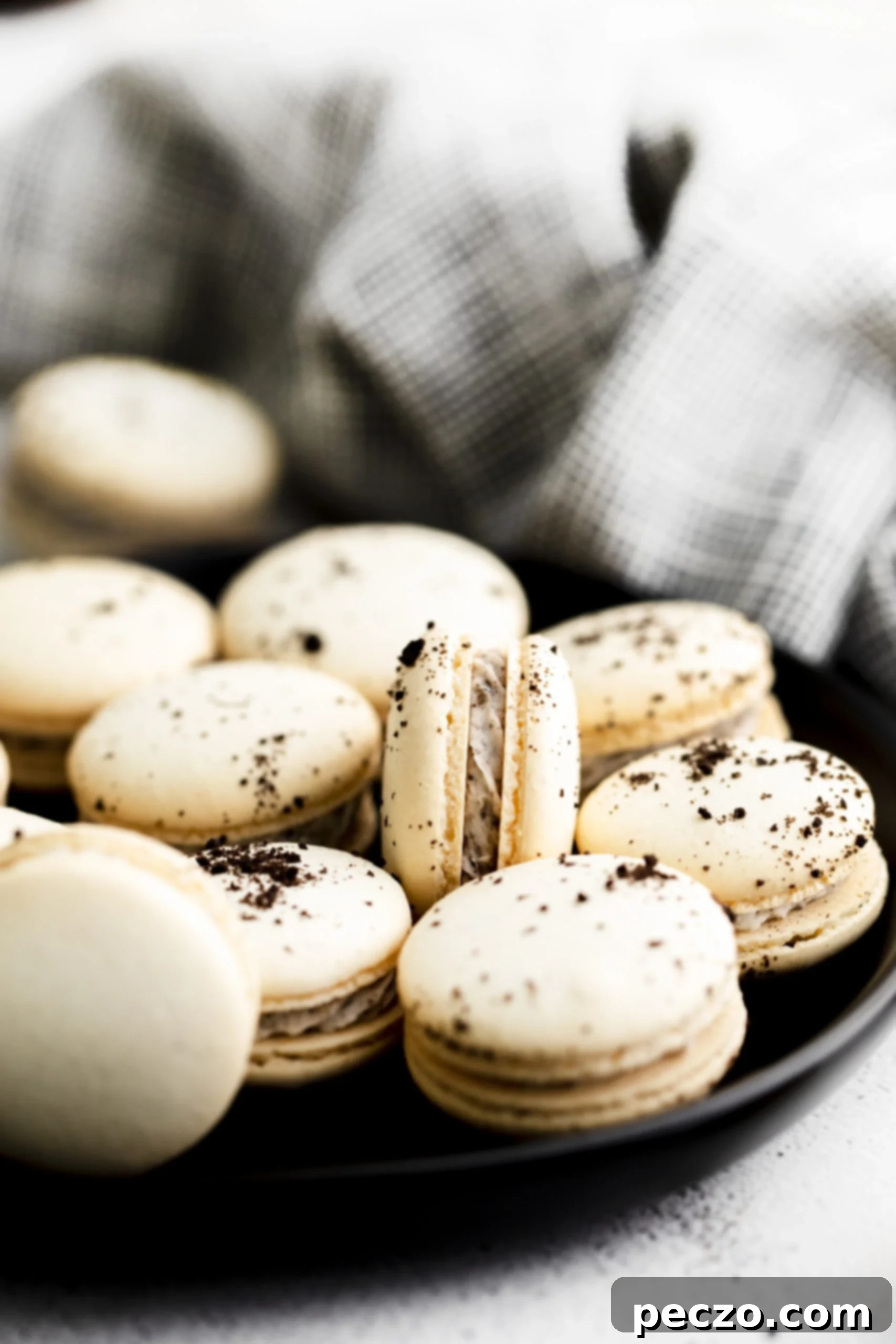 A row of baked cookies and cream macarons cooling on a baking sheet, showcasing their characteristic 'feet'.