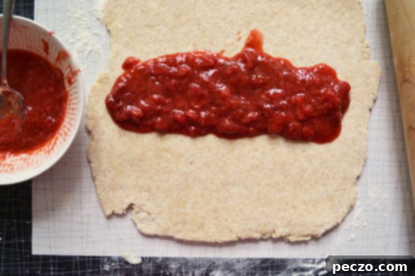 Strawberry rhubarb jam being spread evenly over the rolled-out scone dough, creating a vibrant layer.