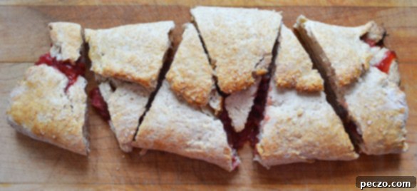 A slice of strawberry rhubarb slab scone revealing flaky layers and a juicy fruit filling, perfect for a treat.