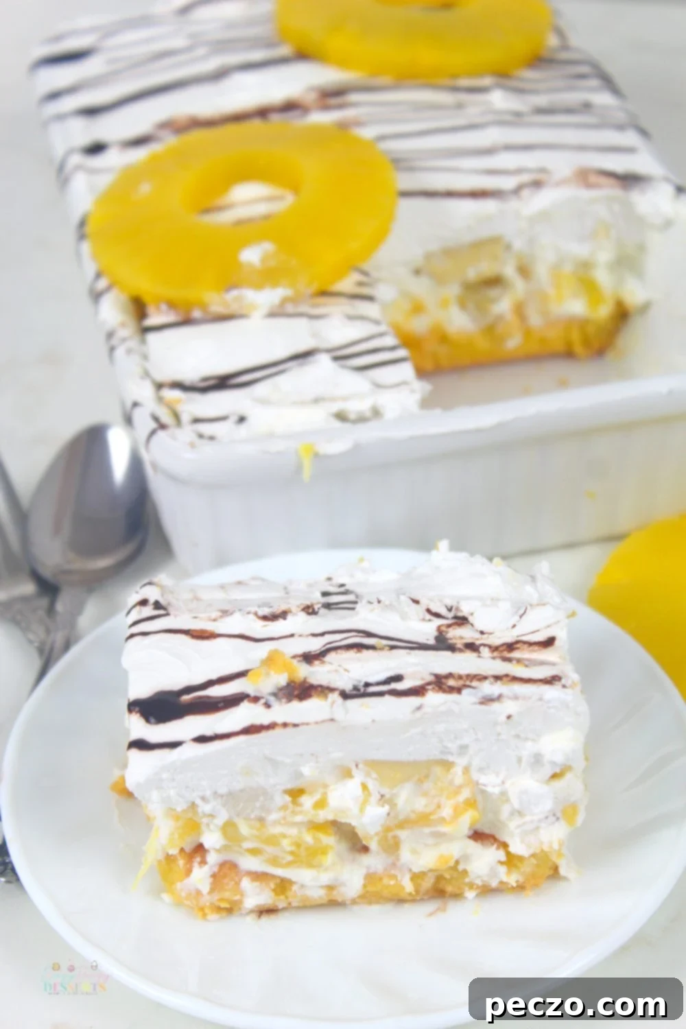 Image of a slice of no bake banana split dessert in a white plate next to a white baking dish filled with the rest of the dessert