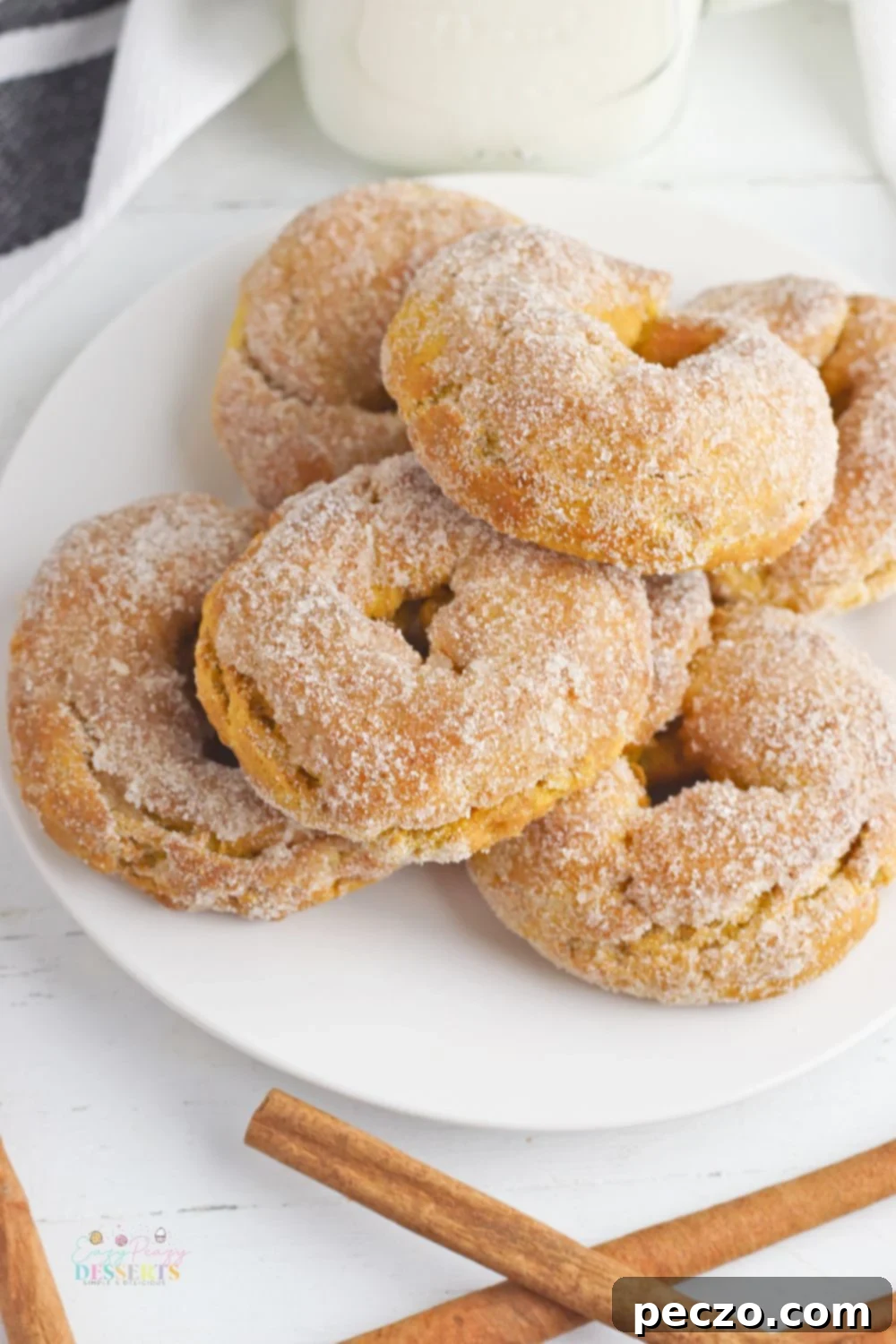 Pumpkin spice donuts on a white serving plate with cinnamon sticks on the side