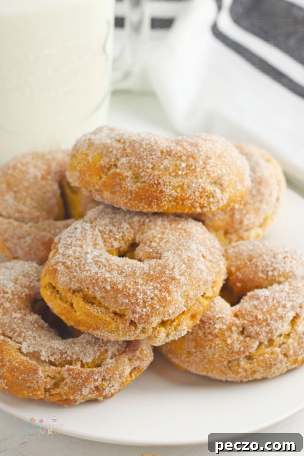 Air fryer pumpkin donuts on a white serving plate next to a glass of milk