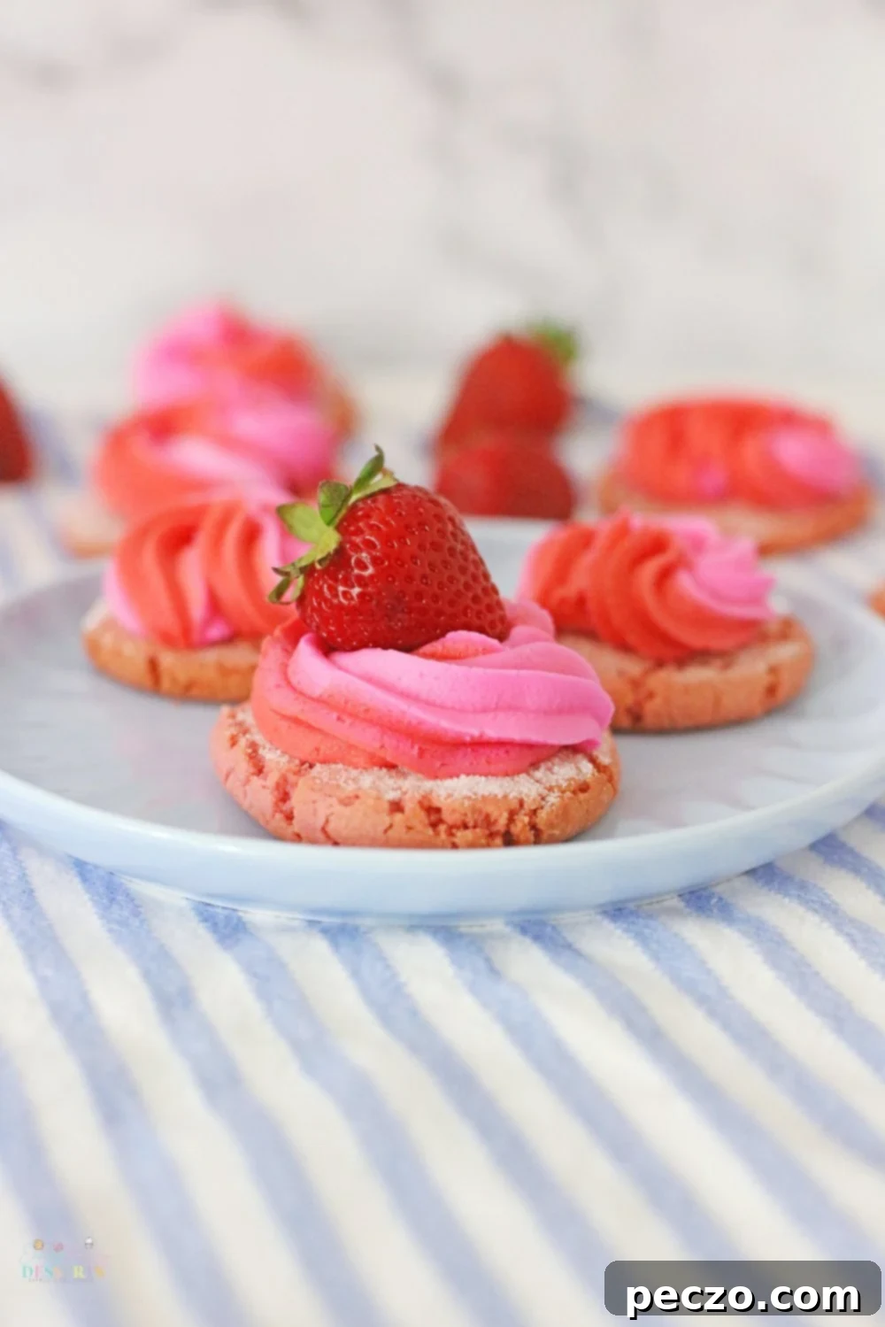 Close up image of a perfectly piped strawberry cream cookie with a fresh strawberry slice on top, resting on a white serving plate