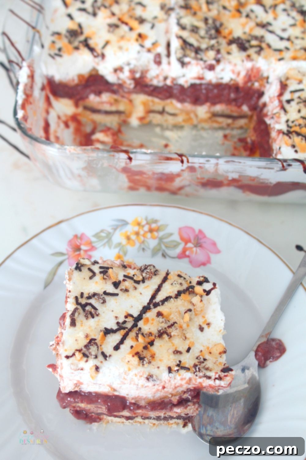 A serving of chocolate peanut butter lasagna in a dessert plate next to a baking dish filled with chocolate lasagna, ready to be served.