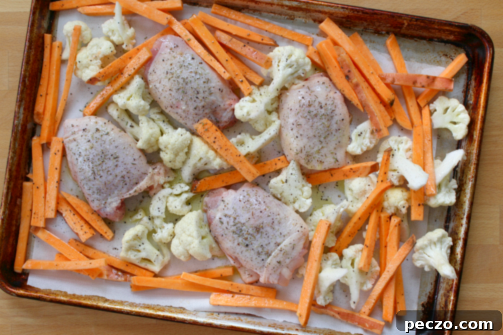 Close-up of crispy skin chicken thighs roasting on a sheet pan with broccoli and potatoes