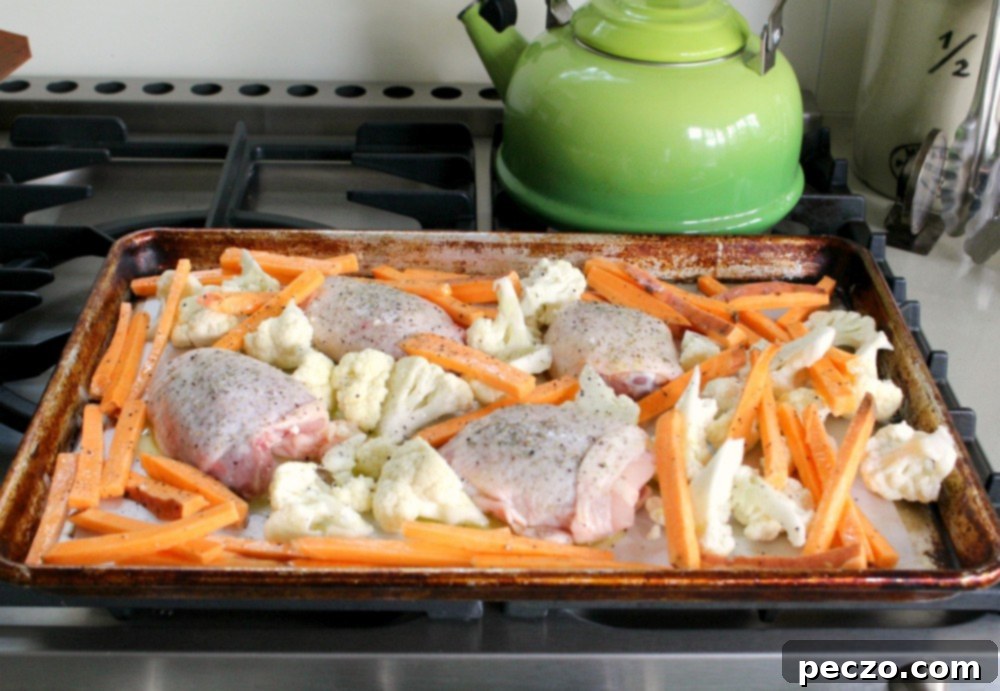 A selection of raw chicken thighs, broccoli florets, and potato wedges arranged on a baking sheet before roasting