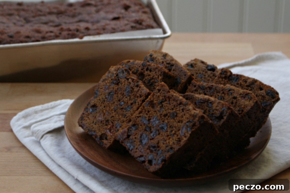 A close-up of a slice of gingerbread fruitcake, revealing the dense texture and abundance of dried fruits.