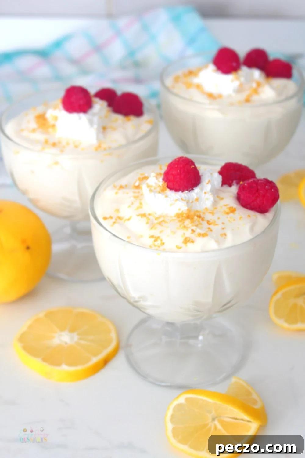 Image of three ice cream cups, filled with lemon mousse, decorated with raspberries, whipped cream, lemon zest and lemon slices