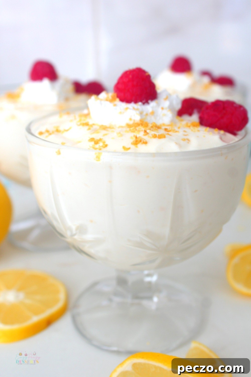 Close up image of lemon cheesecake mousse served in an ice cream cup and decorated with raspberries, lemon zest and whipped cream