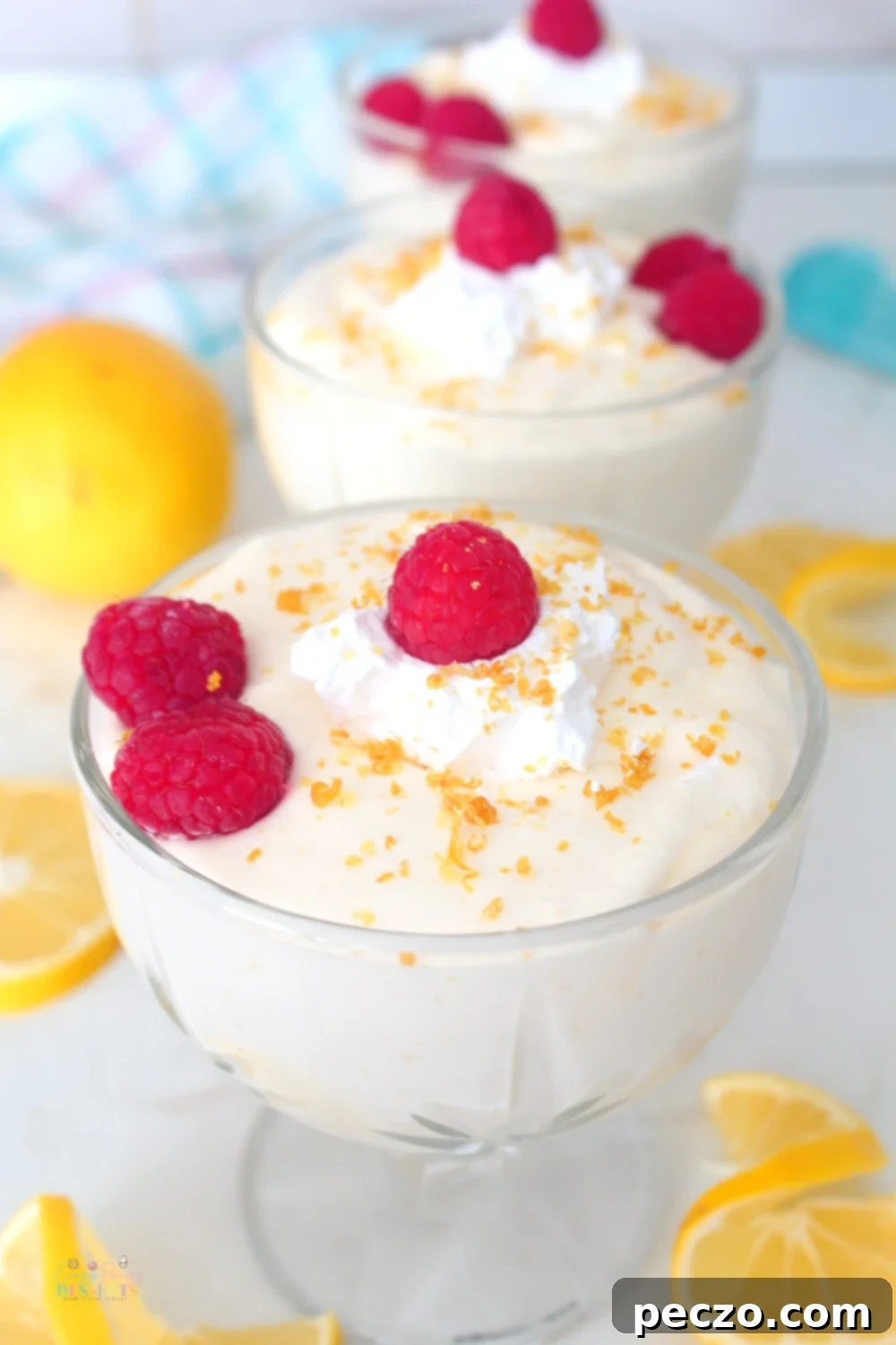 Easy lemon mousse in ice cream cups, garnished with raspberries, lemon zest and a dollop of whipped cream