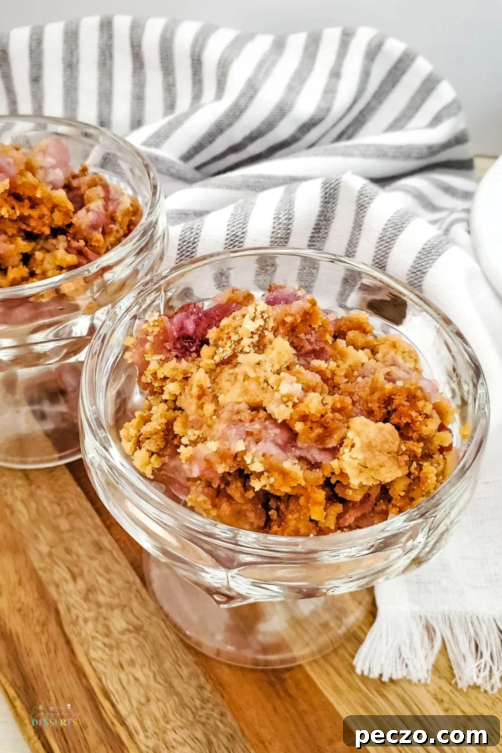 Several glasses of cherry pineapple dump cake, individually portioned, garnished with whipped cream and fresh cherries, on a rustic wooden table.