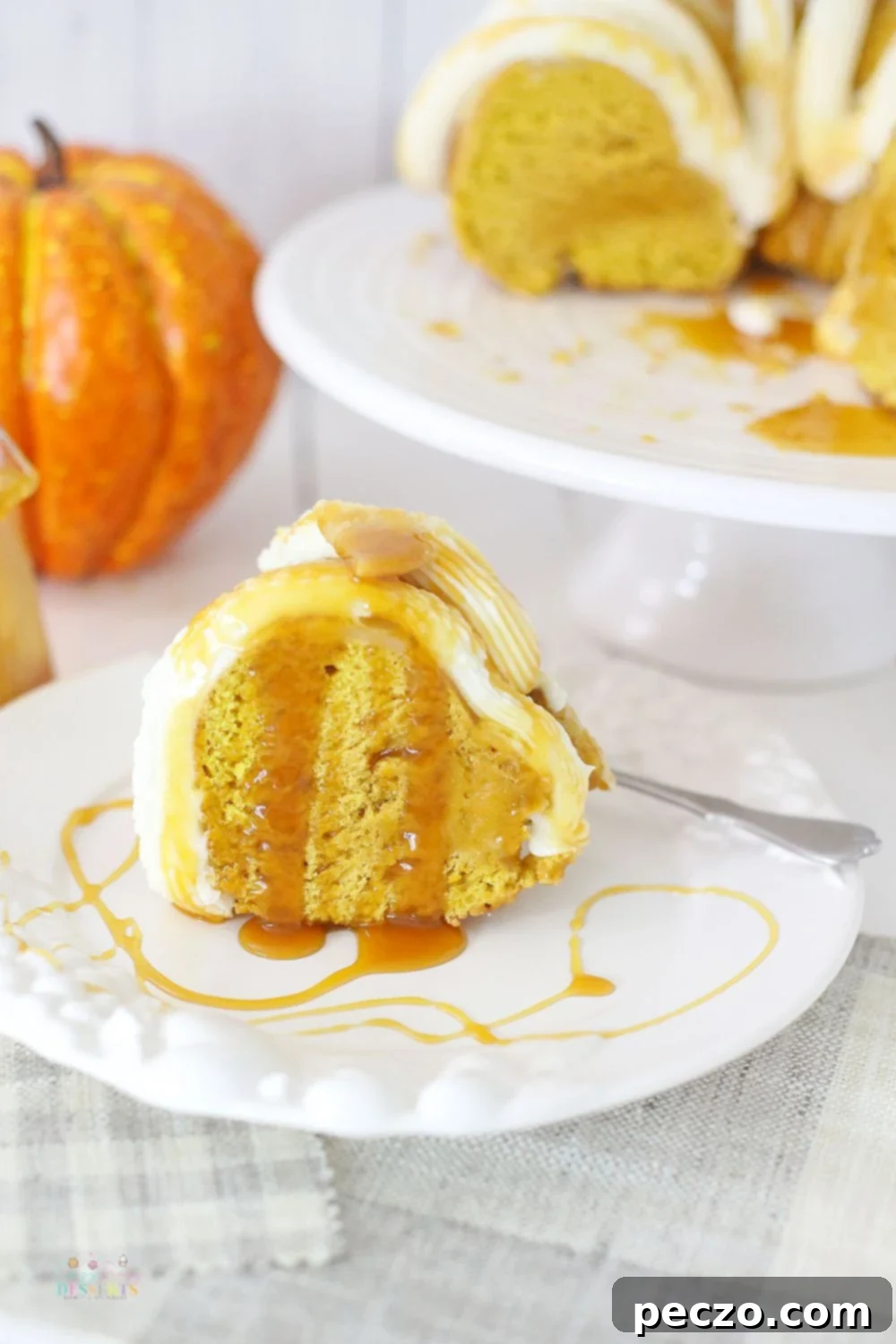 Close up image of a slice of pumpkin bundt cake with buttercream frosting, drizzled with caramel sauce