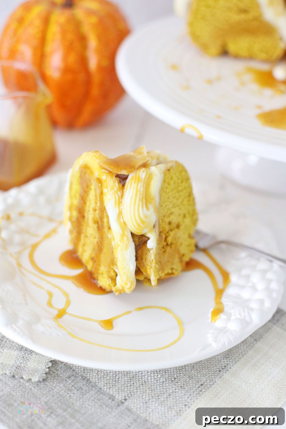 Image of a slice of pumpkin cake with fresh pumpkin, topped with buttercream frosting and drizzled with caramel sauce