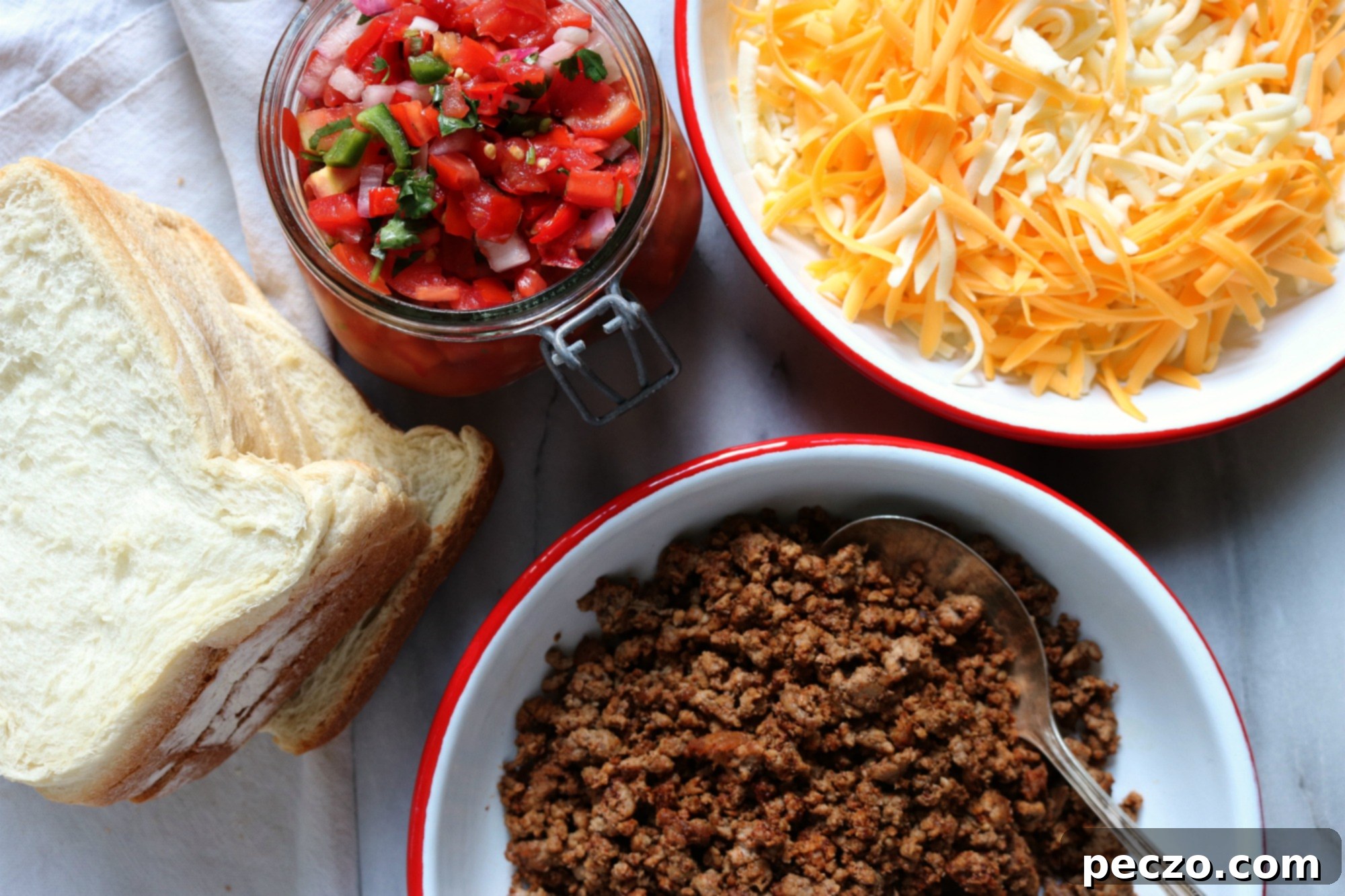 Ingredients for a taco sandwich laid out: slices of bread, a bowl of seasoned ground beef, grated cheese, salsa, and a knife, ready for assembly.