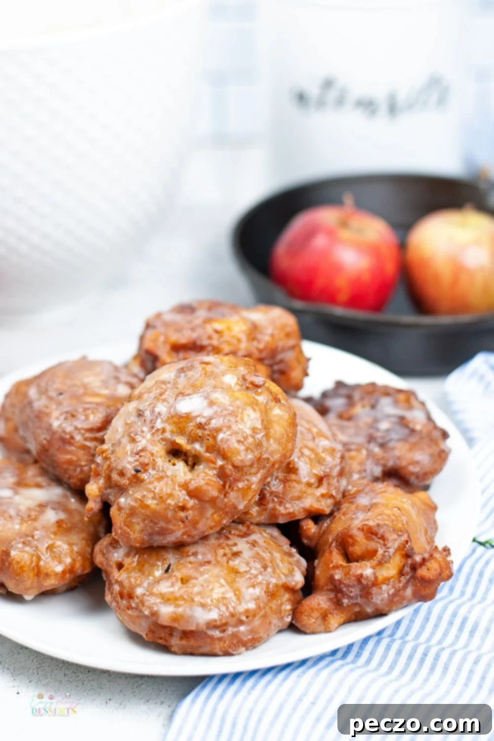 Close up image of golden fried homemade apple fritters with glistening vanilla glaze, ready to be enjoyed