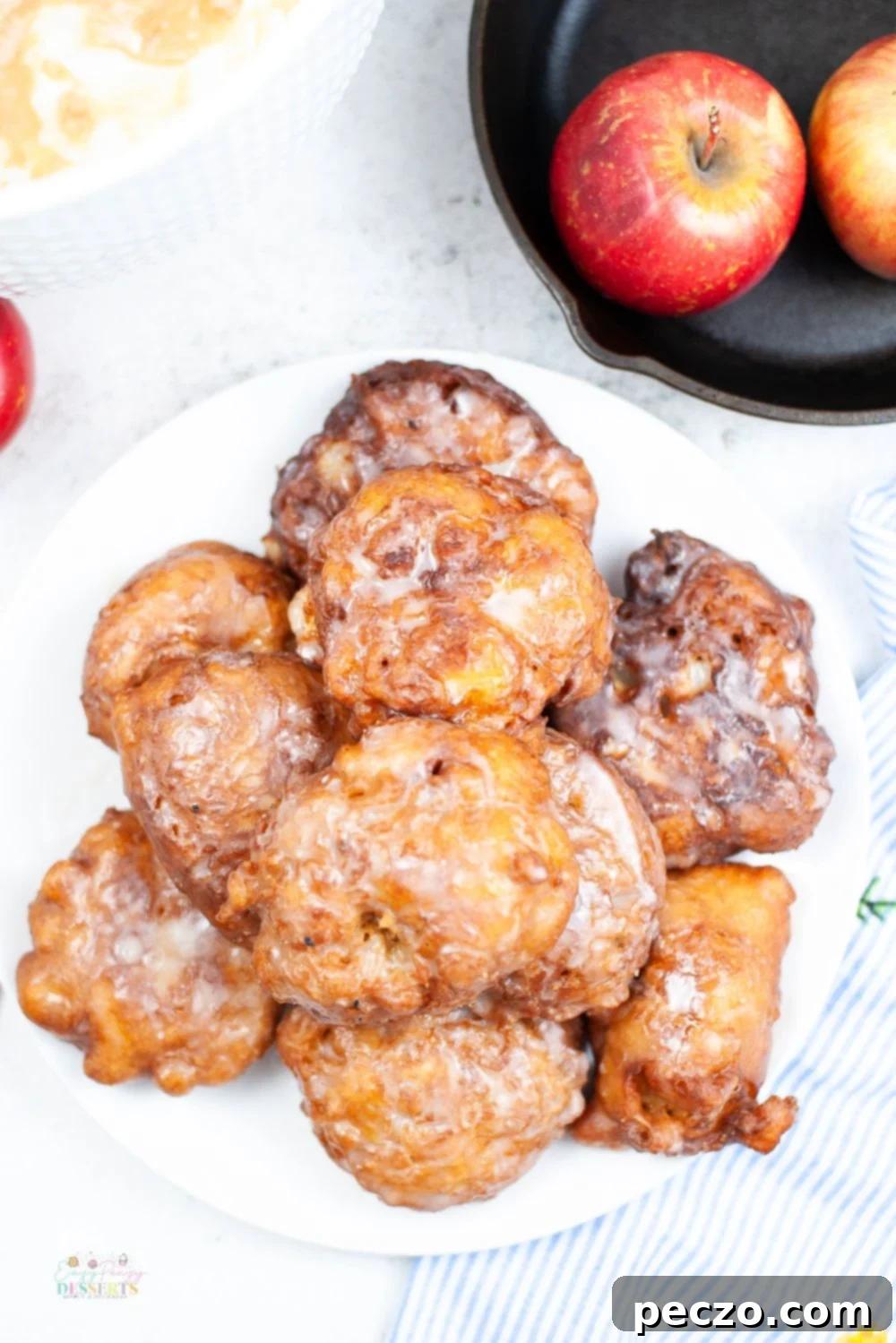 Overhead shot of freshly made easy homemade apple fritters, generously coated with vanilla glaze, on a clean white serving platter