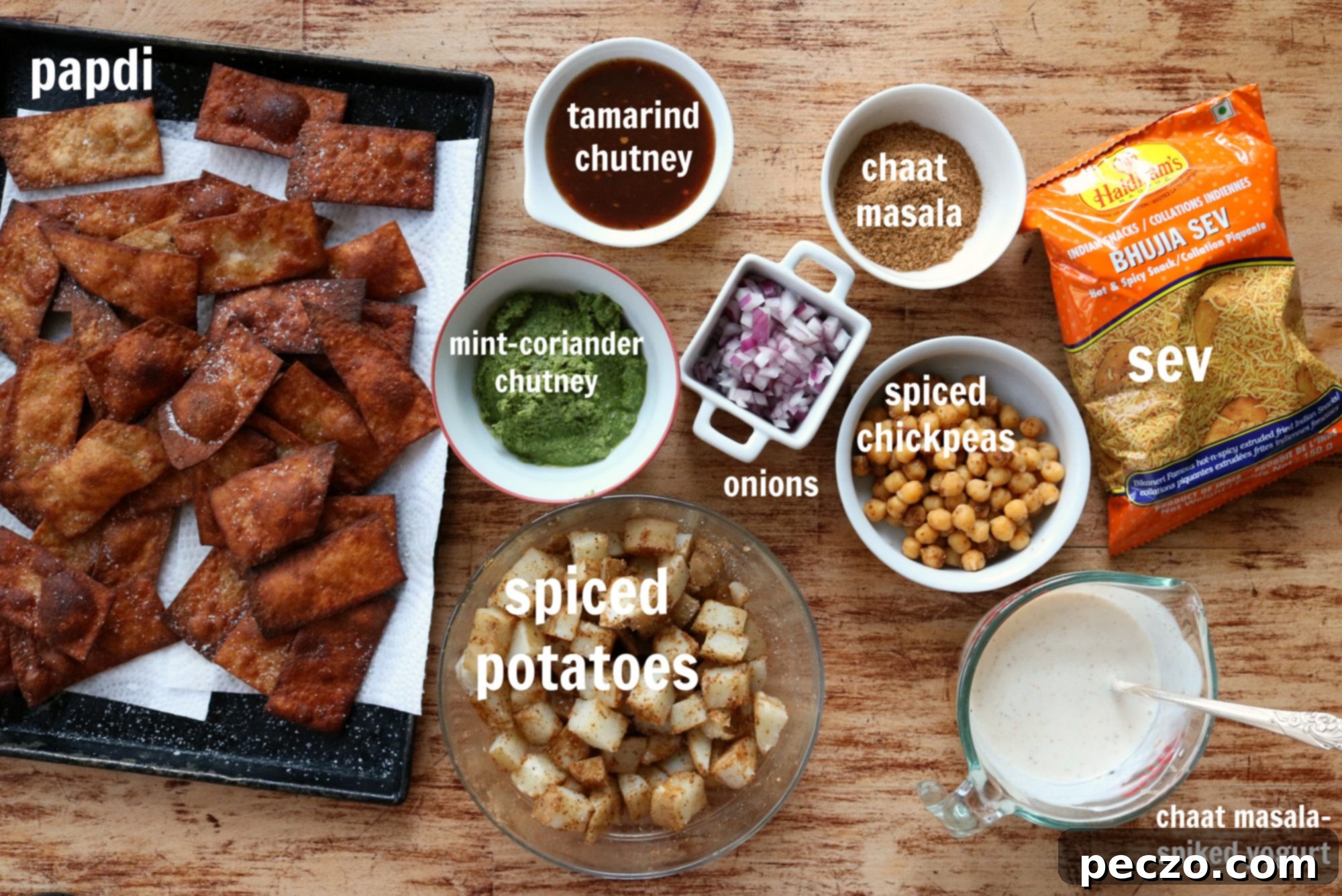 Various ingredients for Papdi Chaat, including spices, chutneys, papdi, and garnishes, laid out on a table with text.