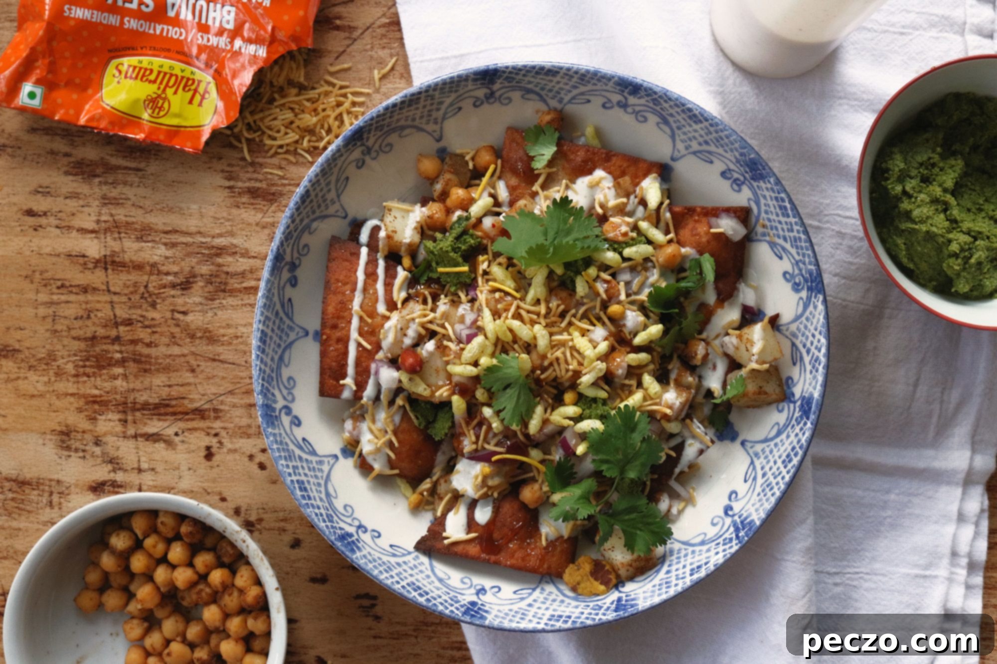 A close-up shot of Papdi Chaat being assembled, showing the layers of papdi, chickpeas, potatoes, and chutneys.