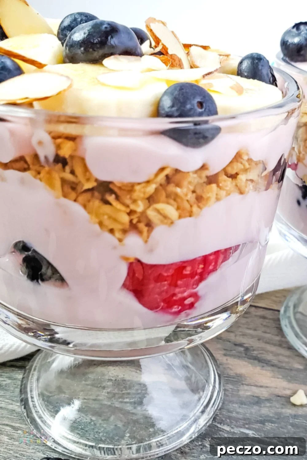 Close up image of mixed berry trifle with granola and banana layers, artfully presented.