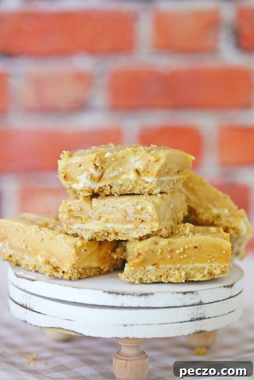 A few squares of no bake peanut butter fudge with cream cheese and a graham crust, stacked up on a wooden dessert plate, ready to be enjoyed.