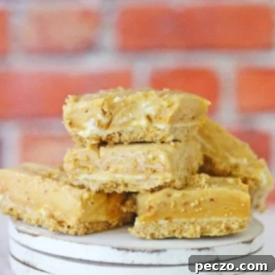 A few squares of no bake peanut butter fudge with cream cheese and a graham crust, stacked up on a wooden dessert plate, ready to be served.