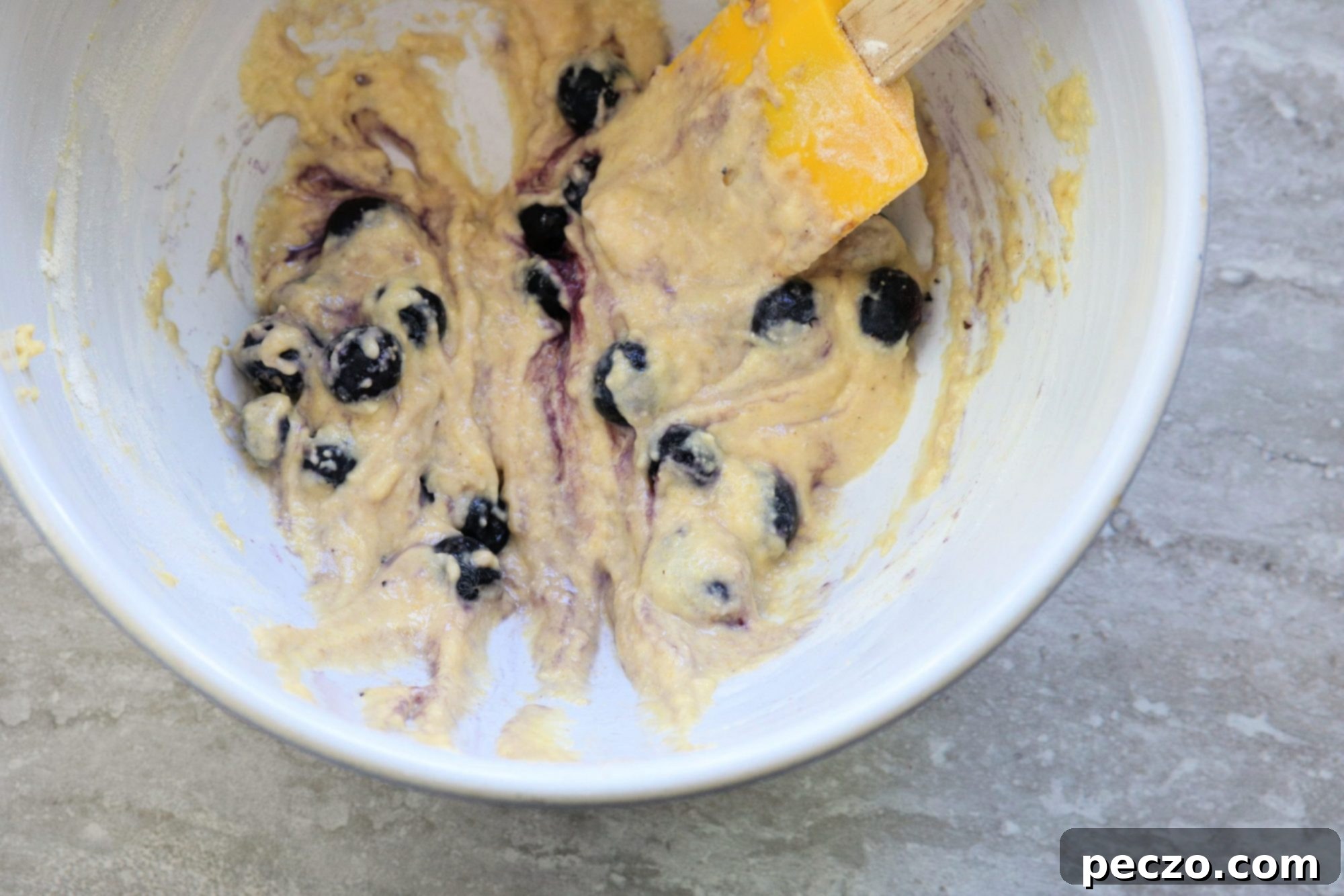 A close-up of golden brown blueberry corn fritters being scooped out of hot oil with a slotted spoon.