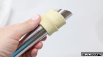 Puff pastry strip being wrapped around a cream horn mold.
