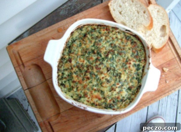Creamy, golden baked spinach and artichoke dip served with tortilla chips and fresh vegetables on a rustic table.