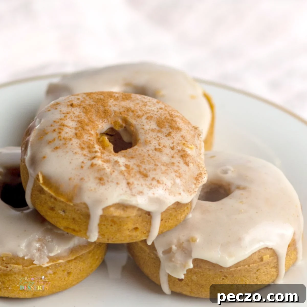 Close up image of perfectly golden vegan pumpkin spice donuts with a generous drizzle of maple glaze, highlighting their fluffy texture.