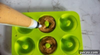 Piping vegan pumpkin donut batter into a donut pan.
