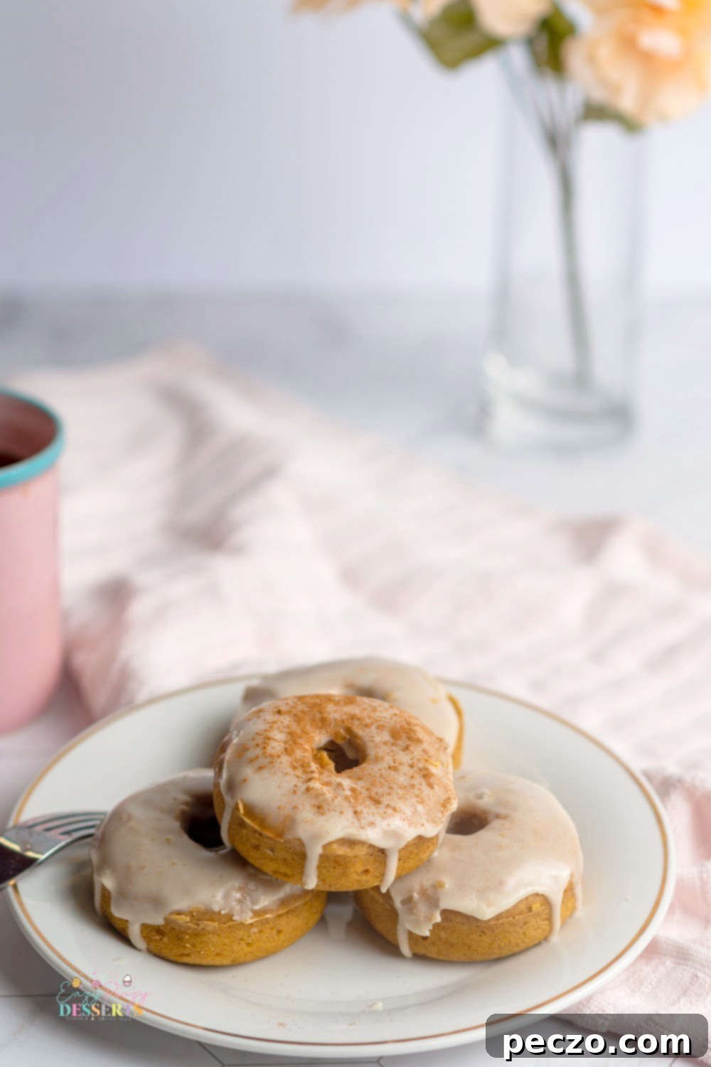 Three perfectly glazed vegan pumpkin donuts arranged artfully on a white serving plate, ready to be enjoyed.