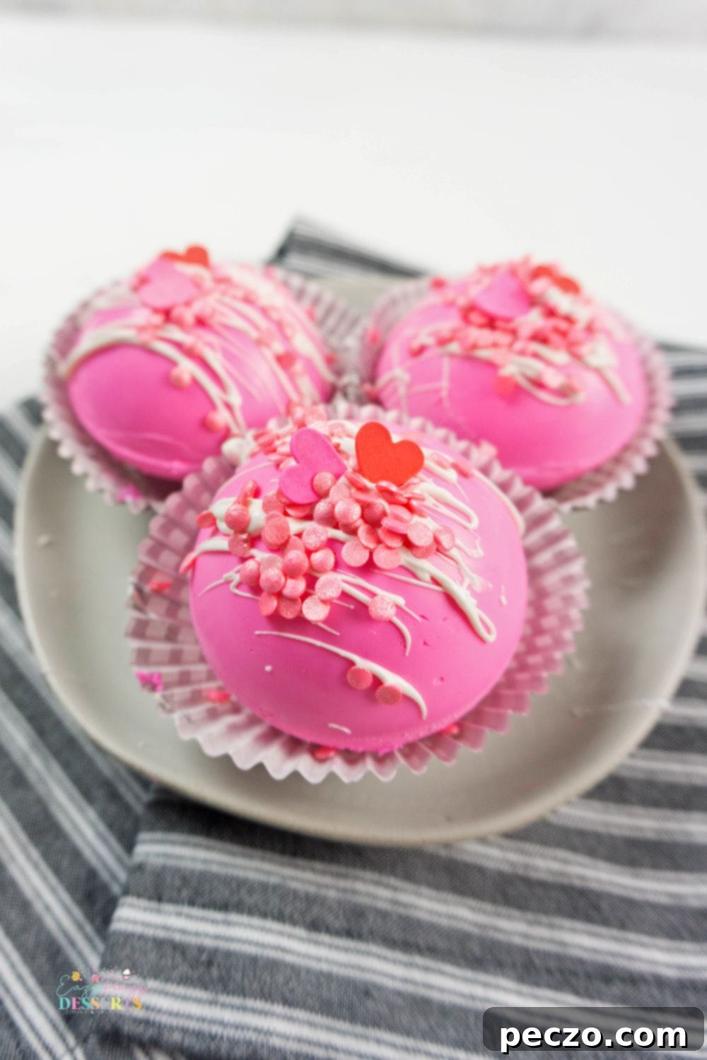 Image of three pink strawberry chocolate bombs on a dessert plate