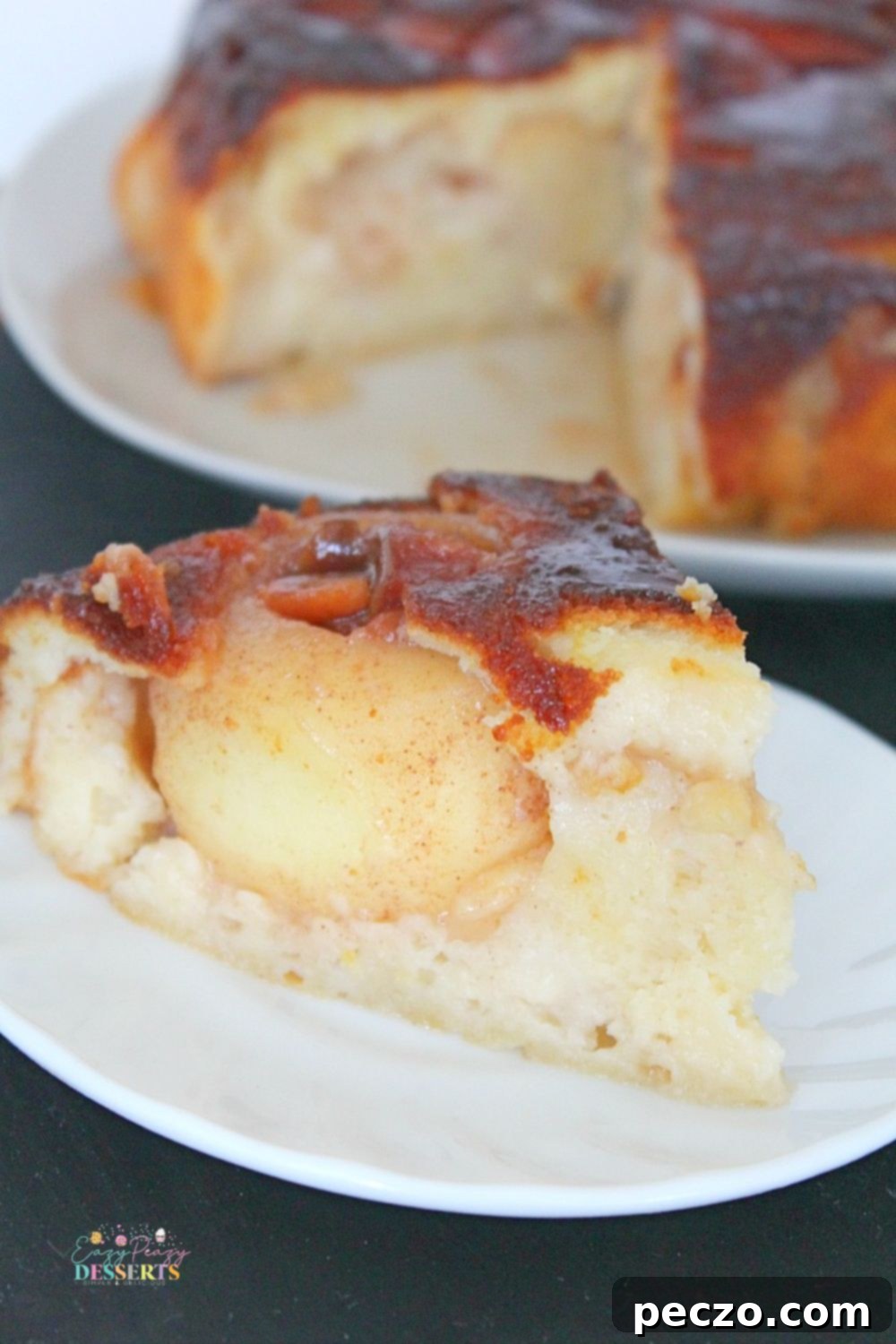 Image of a slice of caramel upside down apple cake on a white plate, showing the layers
