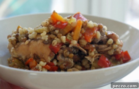 A slow cooker filled with chicken thighs, carrots, celery, red pepper, garlic, lentils, and barley, simmering gently.