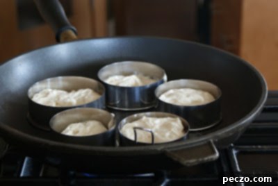 Pierre's Signature Crumpets 4 Crumpet batter cooking within metal rings on a flat-top griddle, showing early bubbling