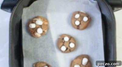 Hot cocoa cookies baking in an air fryer, topped with marshmallows