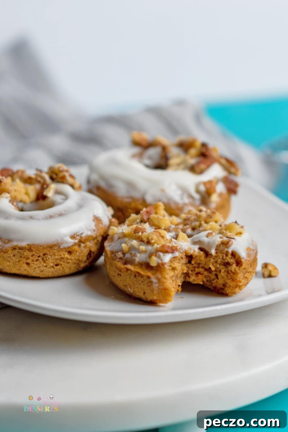 Delicious baked carrot cake donuts topped with cream cheese frosting, walnuts, and pecans.