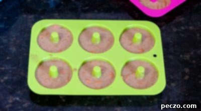 Donut batter being piped into a donut pan using a ziplock bag.