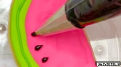 Piping black icing dots and pulling them into watermelon seed shapes