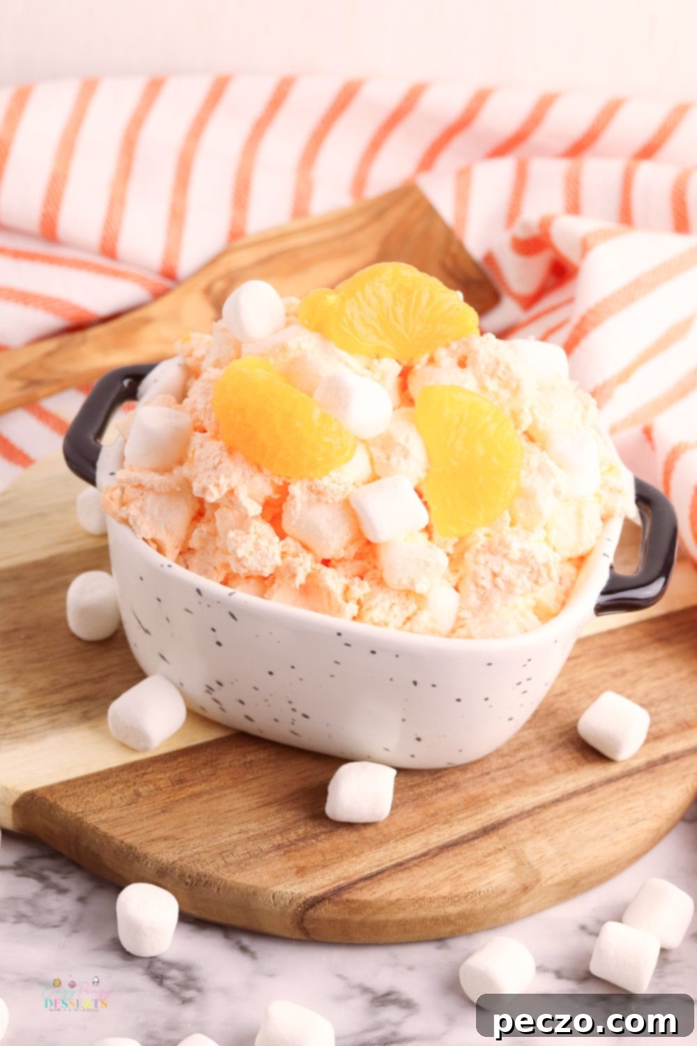 A bowl of orange creamsicle fluff garnished with an orange slice and mint