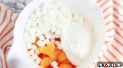 Mixing whipped topping, mandarin oranges, and marshmallows into orange gelatin for fluff salad