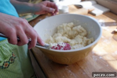A woman's hands expertly mixing perogy dough in a large ceramic bowl, a crucial first step in crafting tender, authentic Ukrainian dumplings from scratch.